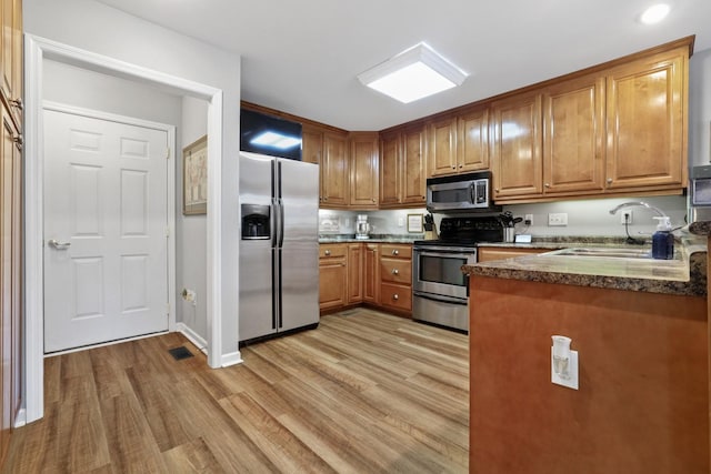 kitchen featuring light hardwood / wood-style floors, sink, appliances with stainless steel finishes, and dark stone countertops