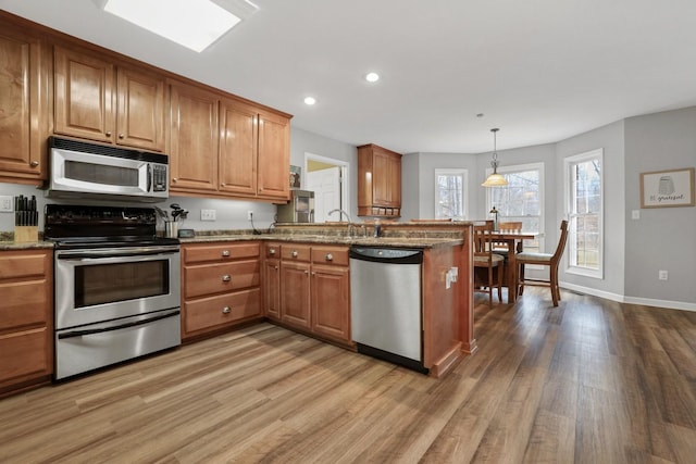 kitchen with pendant lighting, kitchen peninsula, hardwood / wood-style flooring, and stainless steel appliances