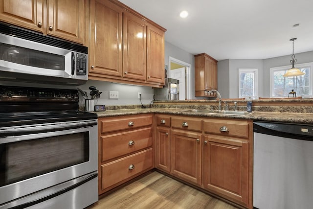 kitchen featuring appliances with stainless steel finishes, light wood-type flooring, dark stone countertops, hanging light fixtures, and sink