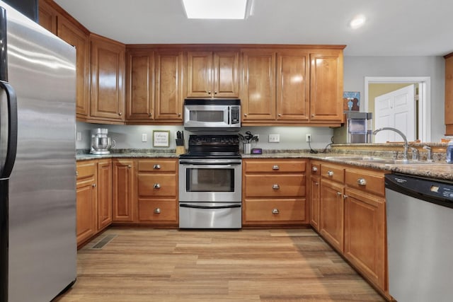 kitchen featuring stainless steel appliances, light hardwood / wood-style flooring, light stone counters, and sink