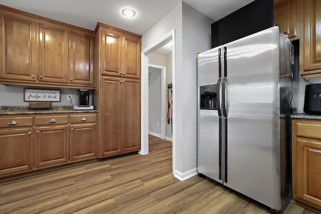 kitchen with stainless steel fridge with ice dispenser, dark stone countertops, and hardwood / wood-style floors