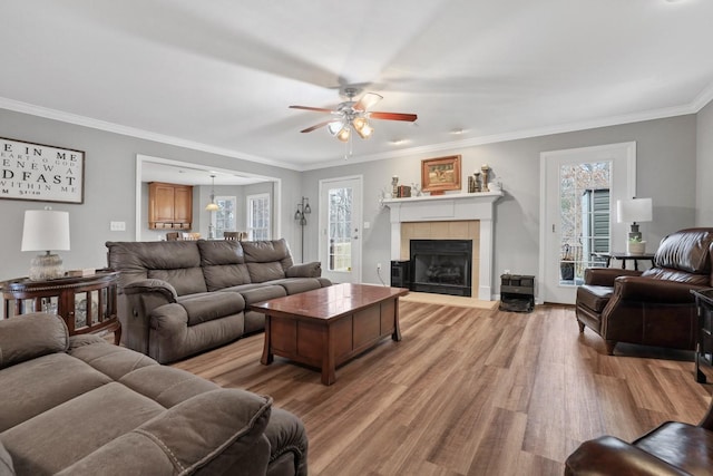 living room featuring light hardwood / wood-style floors, a tile fireplace, crown molding, and ceiling fan