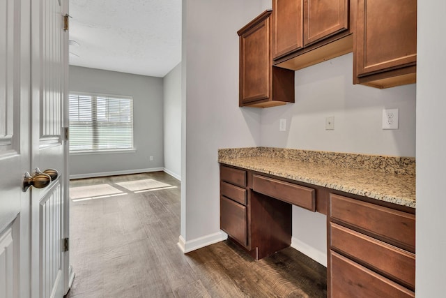 kitchen with dark hardwood / wood-style flooring, built in desk, and light stone countertops