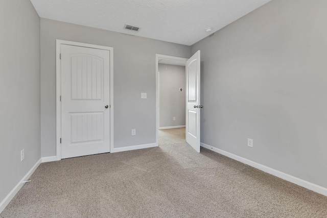 unfurnished bedroom featuring light colored carpet, a textured ceiling, and a closet