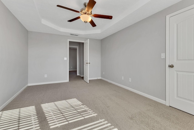 carpeted spare room with ceiling fan, a textured ceiling, and a tray ceiling