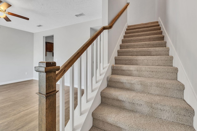 stairway featuring a textured ceiling, ceiling fan, and wood-type flooring