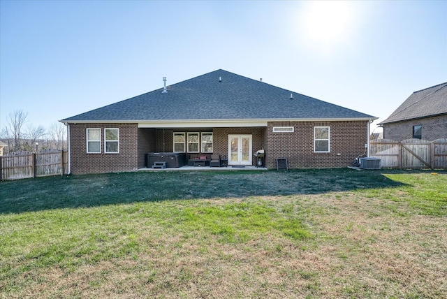 rear view of house with french doors, cooling unit, a hot tub, and a lawn