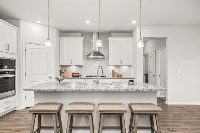 kitchen featuring hanging light fixtures, white cabinets, stainless steel appliances, and a kitchen island with sink