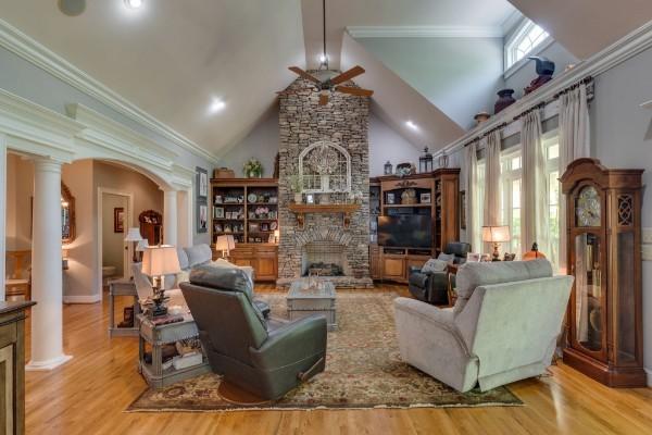 living room with light wood-type flooring, a fireplace, high vaulted ceiling, and decorative columns