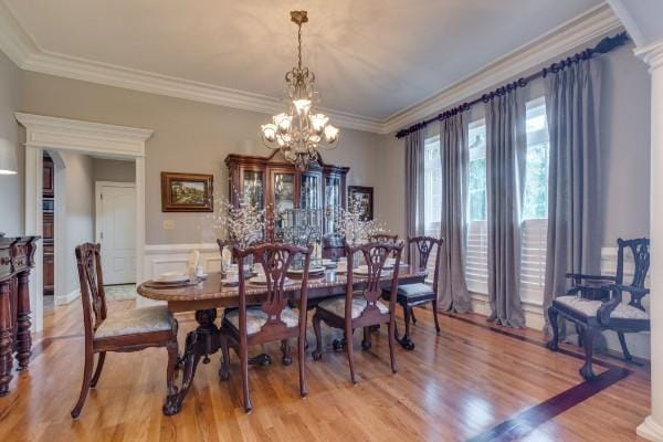 dining area with light hardwood / wood-style floors, crown molding, a chandelier, and decorative columns