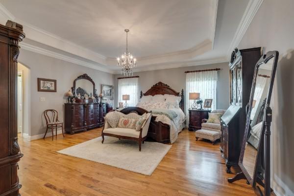 bedroom featuring light wood-type flooring, crown molding, a raised ceiling, and a notable chandelier