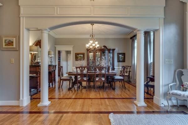 dining room featuring ornate columns, ornamental molding, hardwood / wood-style flooring, and a notable chandelier