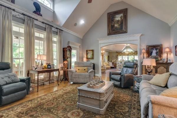 living room with high vaulted ceiling, wood-type flooring, ornamental molding, and ceiling fan