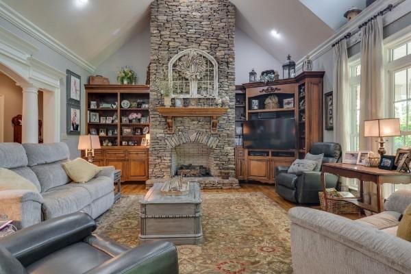 living room featuring high vaulted ceiling, wood-type flooring, a stone fireplace, and decorative columns