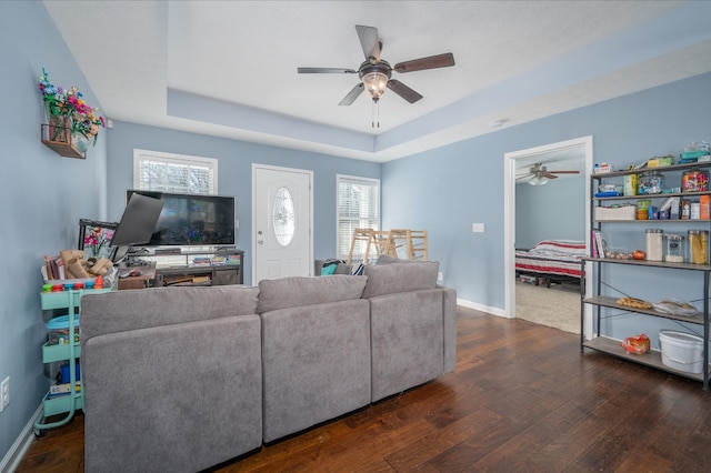 living room featuring dark wood-type flooring, a raised ceiling, and ceiling fan