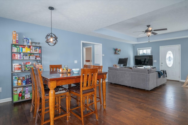 dining area featuring ceiling fan, a tray ceiling, dark hardwood / wood-style flooring, and a textured ceiling