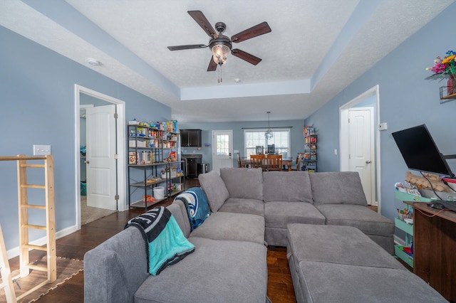 living room featuring ceiling fan, a tray ceiling, dark hardwood / wood-style flooring, and a textured ceiling