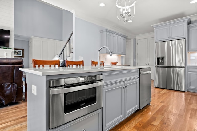 kitchen with sink, stainless steel fridge, gray cabinets, an island with sink, and oven