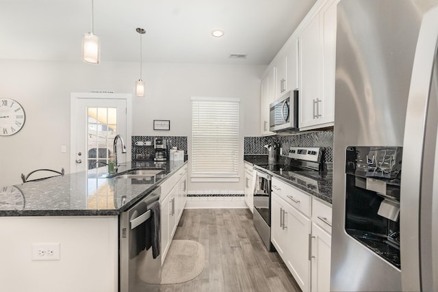 kitchen with decorative light fixtures, white cabinetry, stainless steel appliances, sink, and a kitchen island with sink