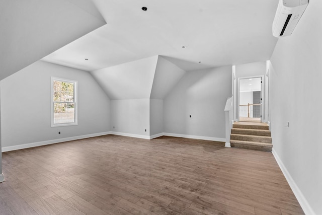 additional living space with light wood-type flooring, a wall mounted air conditioner, and vaulted ceiling