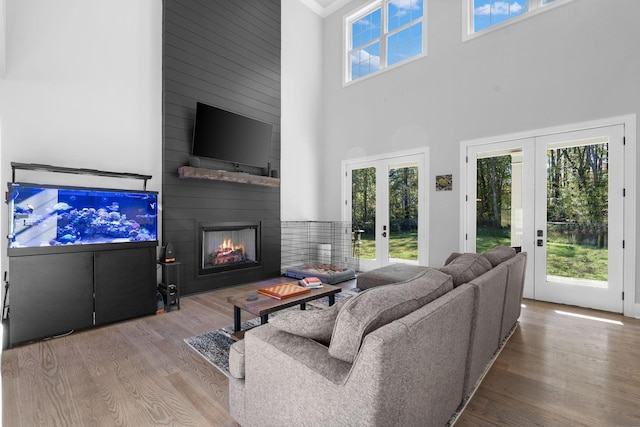 living room featuring light wood-type flooring, french doors, a high ceiling, and a fireplace