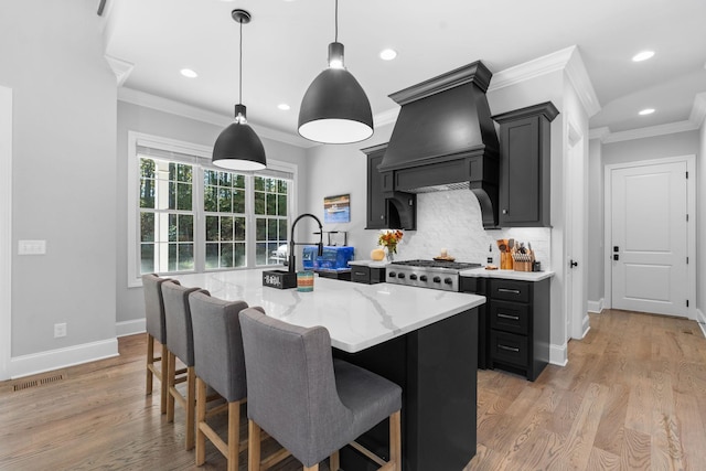 kitchen with an island with sink, custom range hood, backsplash, and decorative light fixtures