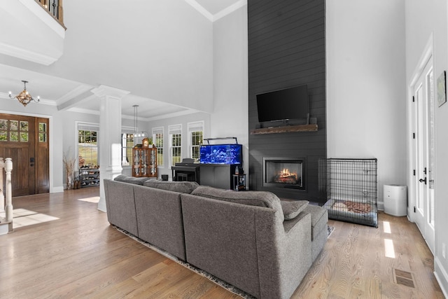 living room featuring light hardwood / wood-style floors, ornamental molding, a large fireplace, decorative columns, and an inviting chandelier