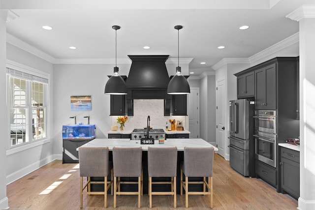 kitchen featuring light hardwood / wood-style floors, pendant lighting, stainless steel appliances, and an island with sink