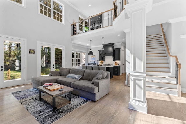 living room with a towering ceiling, french doors, decorative columns, light hardwood / wood-style flooring, and crown molding