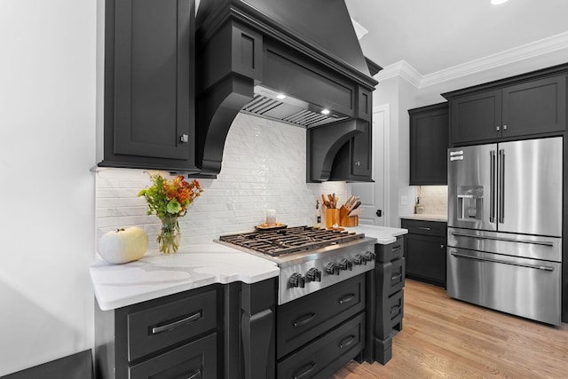 kitchen with light hardwood / wood-style flooring, appliances with stainless steel finishes, premium range hood, backsplash, and ornamental molding