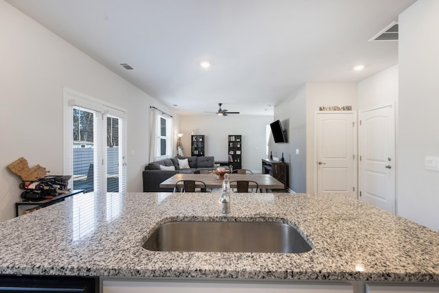 kitchen with sink, ceiling fan, light stone counters, and a kitchen island with sink