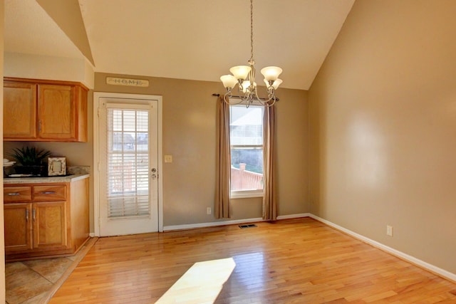 unfurnished dining area featuring lofted ceiling, an inviting chandelier, and light wood-type flooring