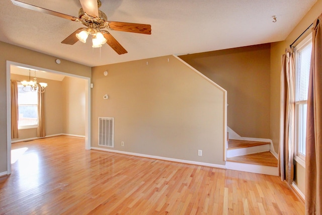 empty room featuring ceiling fan with notable chandelier and light hardwood / wood-style floors