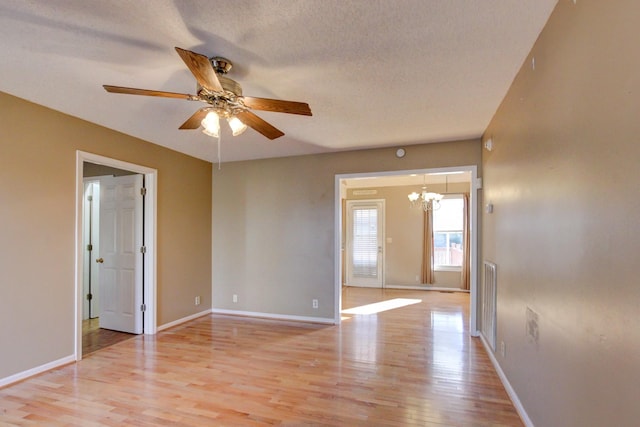 spare room featuring ceiling fan with notable chandelier, a textured ceiling, and light wood-type flooring