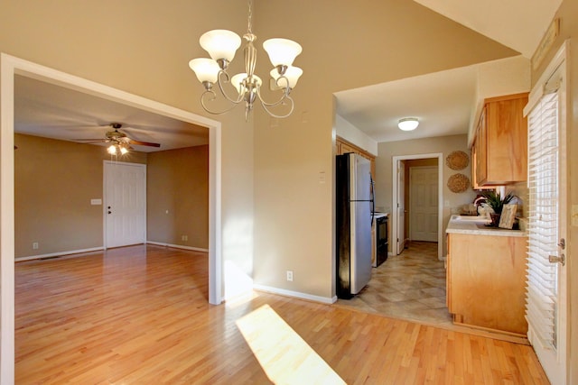 kitchen featuring sink, hanging light fixtures, light wood-type flooring, stainless steel fridge, and ceiling fan with notable chandelier