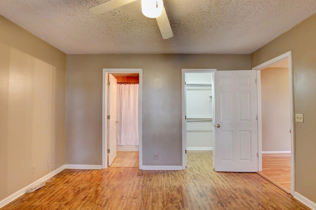 unfurnished bedroom featuring ceiling fan, a spacious closet, a textured ceiling, and ensuite bath