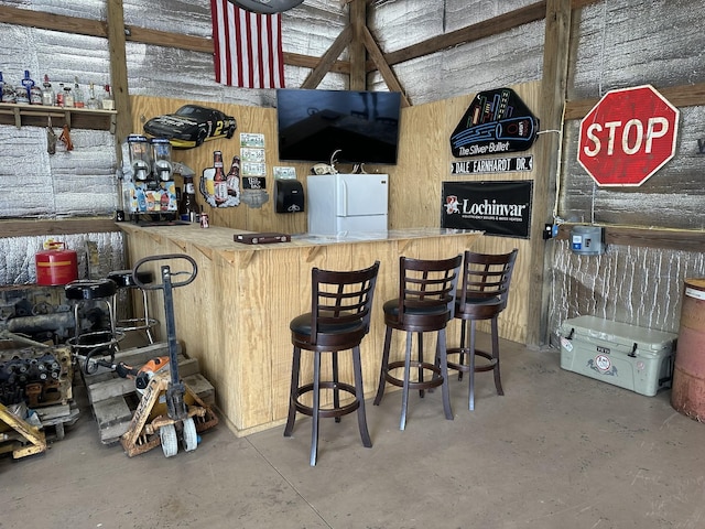 bar with wood walls, white refrigerator, and concrete flooring