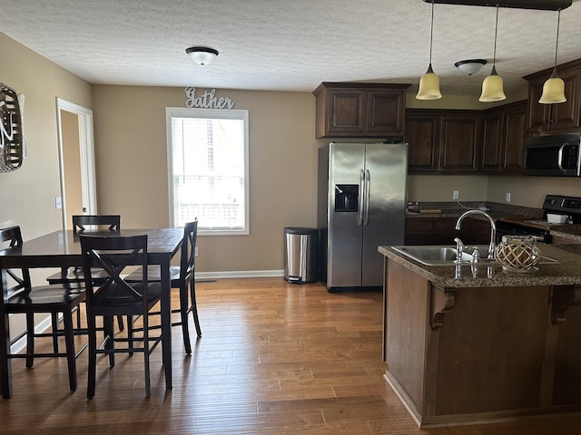 kitchen with a kitchen breakfast bar, appliances with stainless steel finishes, sink, a textured ceiling, and dark stone countertops