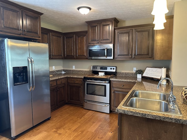 kitchen featuring sink, a textured ceiling, appliances with stainless steel finishes, and light hardwood / wood-style flooring