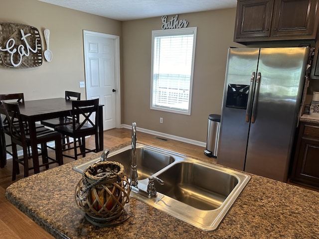 kitchen featuring stainless steel refrigerator with ice dispenser, sink, hardwood / wood-style flooring, dark stone counters, and dark brown cabinetry