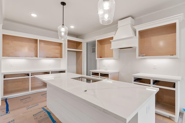 kitchen with custom exhaust hood, a center island, hanging light fixtures, ornamental molding, and light stone counters