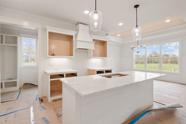 kitchen featuring decorative light fixtures, a healthy amount of sunlight, custom range hood, and an island with sink