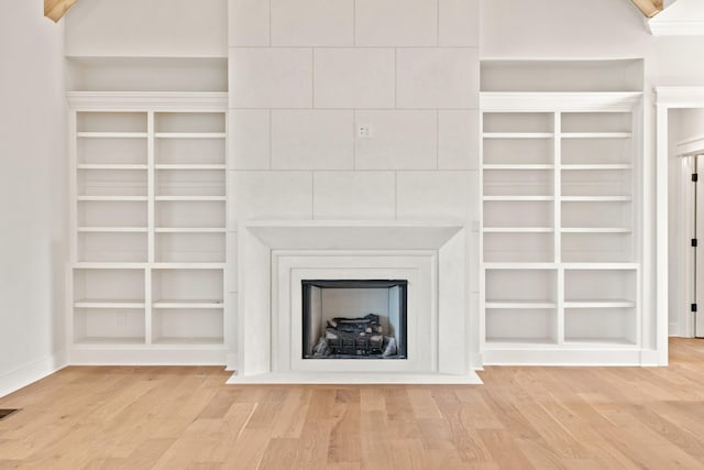 unfurnished living room featuring a large fireplace, visible vents, built in features, and wood finished floors