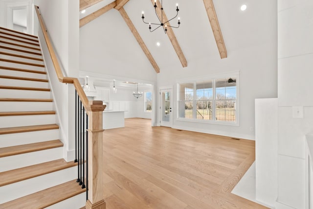 unfurnished living room featuring high vaulted ceiling, stairway, beam ceiling, and an inviting chandelier