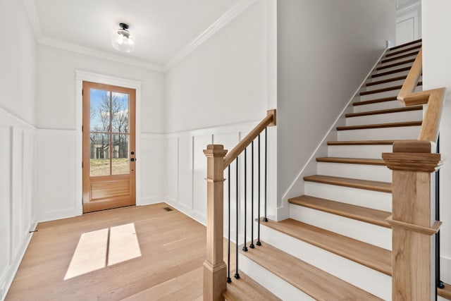 foyer with light wood-style floors, ornamental molding, a decorative wall, and a wainscoted wall