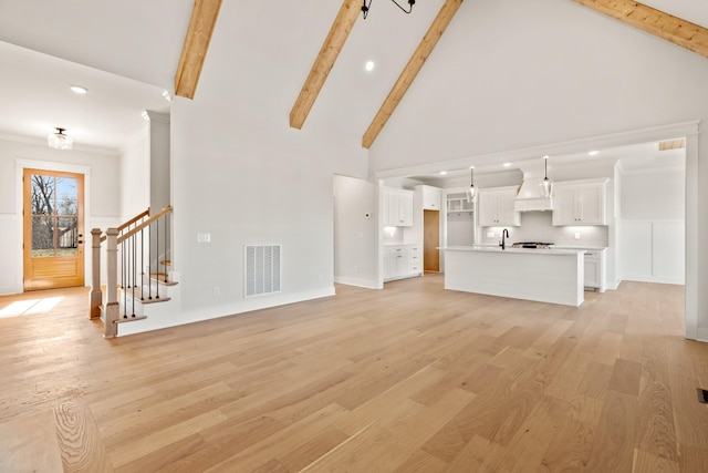 unfurnished living room featuring stairway, visible vents, light wood finished floors, and beamed ceiling