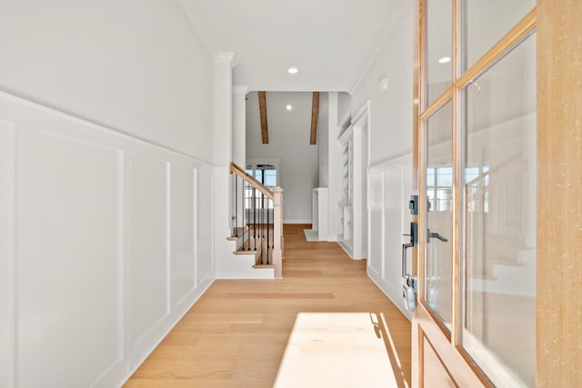 entryway with a towering ceiling, light wood-style flooring, stairs, crown molding, and a decorative wall