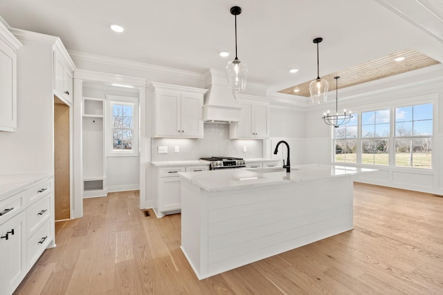 kitchen with premium range hood, a sink, white cabinets, a center island with sink, and decorative light fixtures