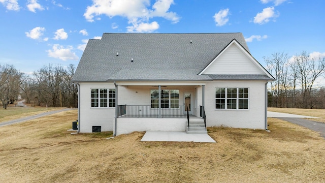 back of property with a ceiling fan, a lawn, roof with shingles, a porch, and brick siding