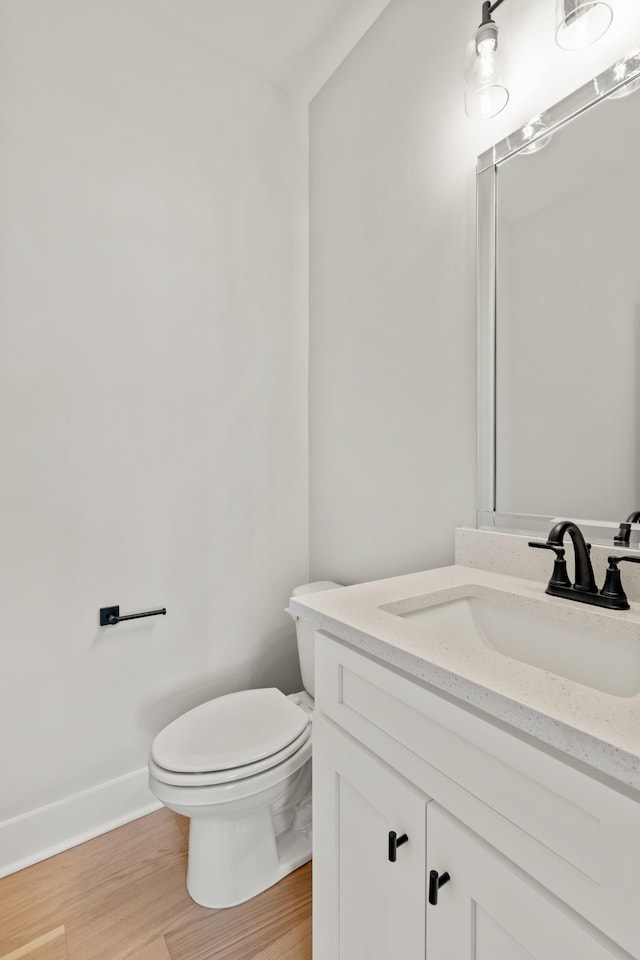 bathroom featuring toilet, baseboards, wood finished floors, and vanity